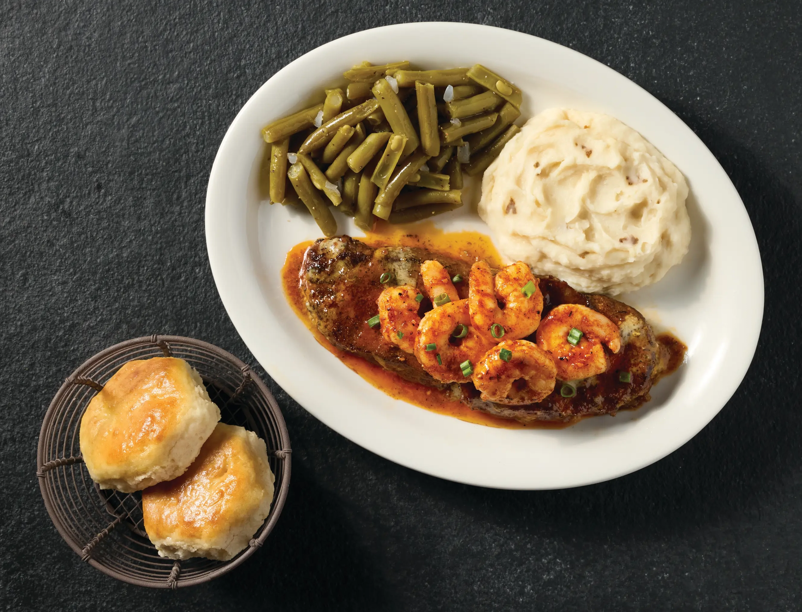 Steak topped with shrimp, served with mashed potatoes, green beans, and biscuits.