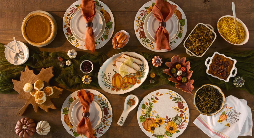 Fall-themed table setting with turkey, sides, biscuits, and pumpkin-inspired dinnerware on a rustic wooden table.